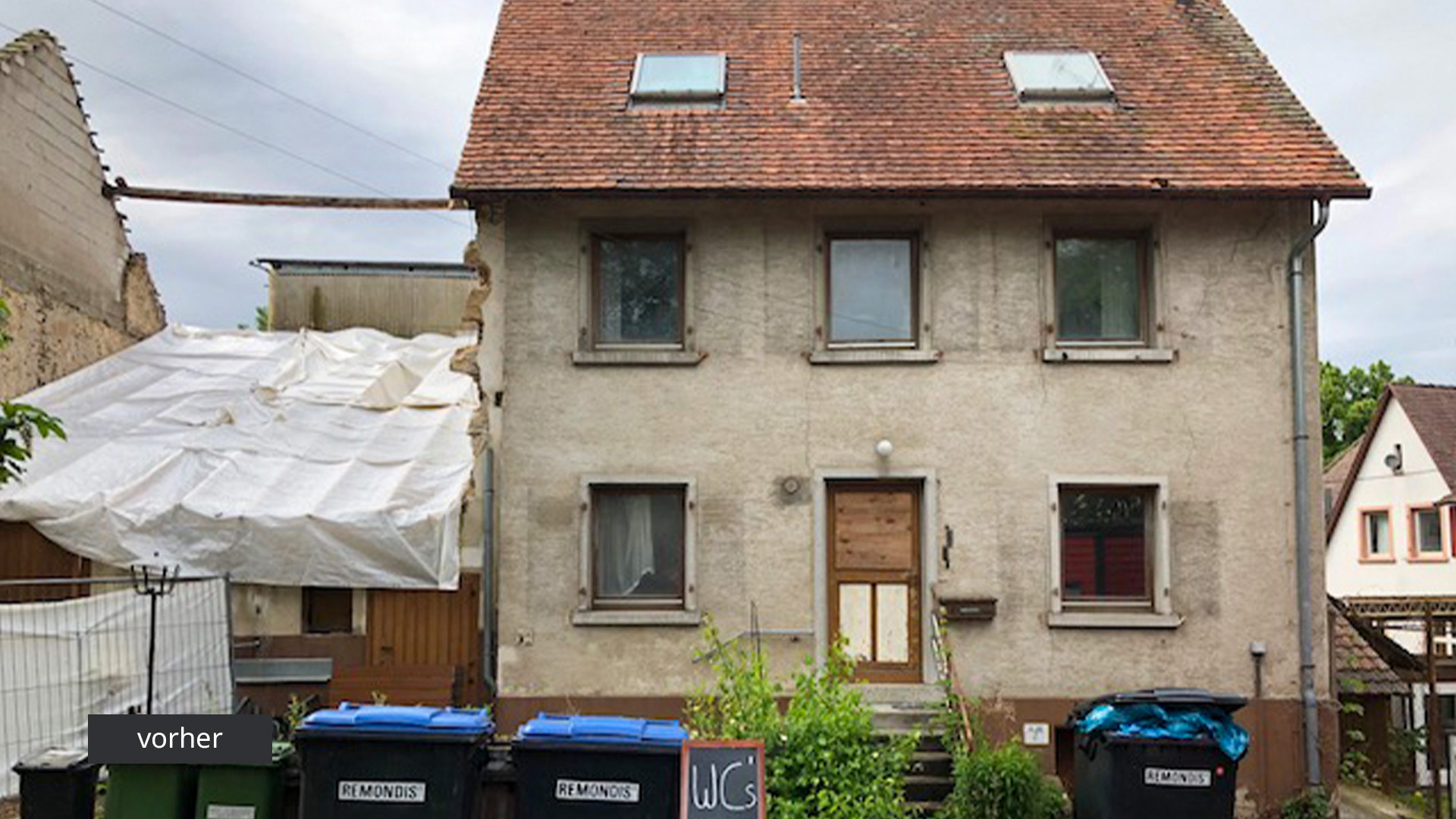 Ansicht eines alten Einfamilienhauses mit Mülltonnen