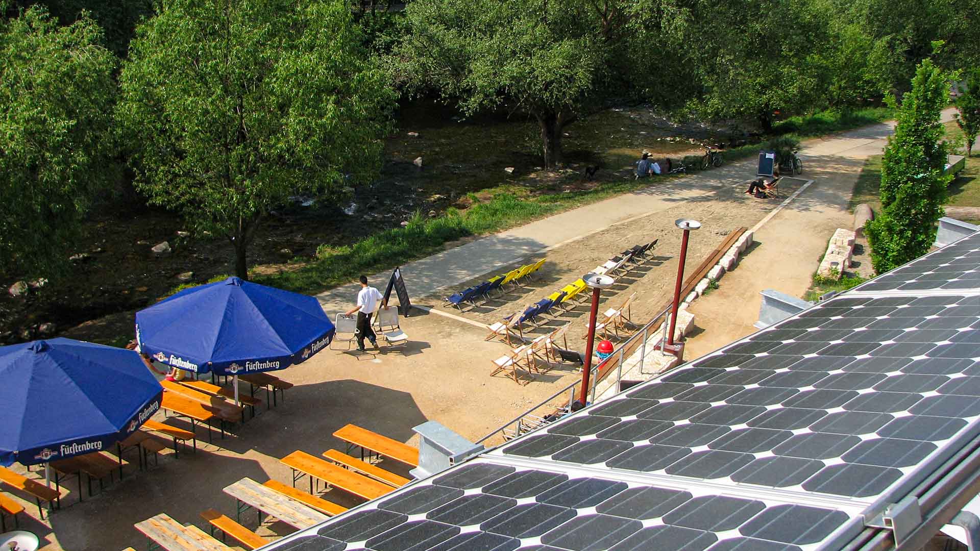 Ansicht von oben auf einen Caféaussenbereich an einem Fluss mit Solaranlage