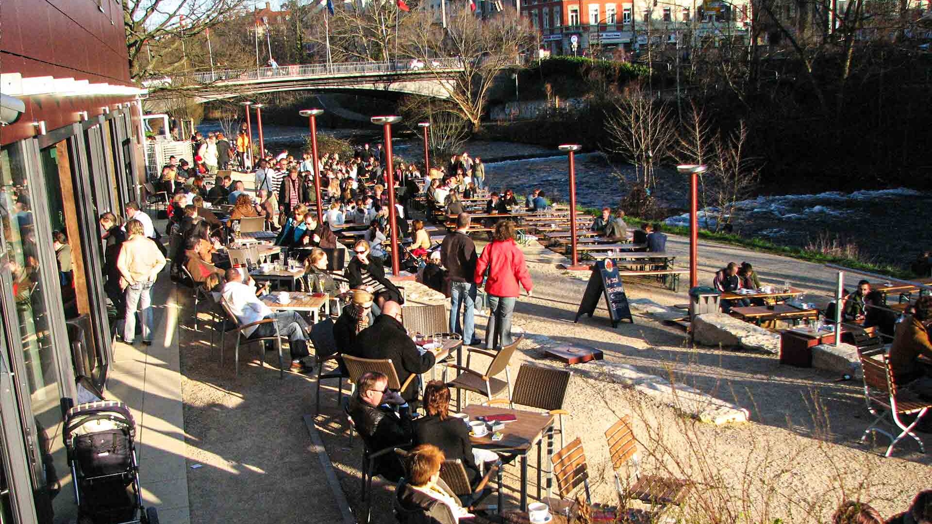 Menschen auf einer Café-Terasse neben einem Fluss