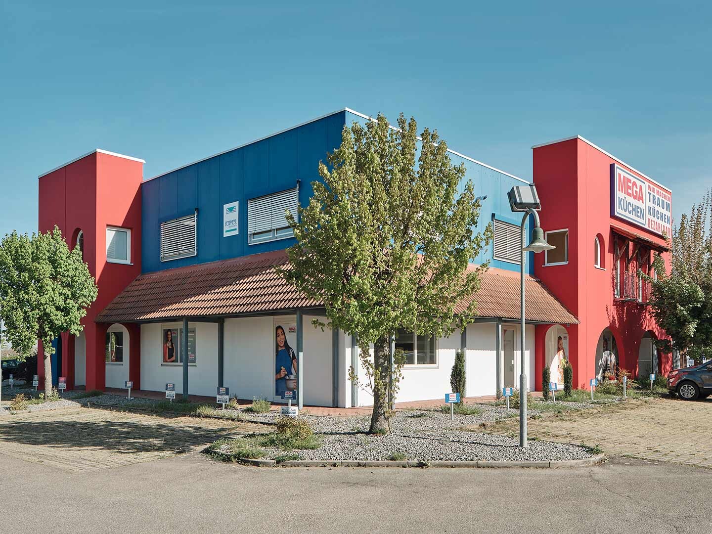 Ansicht auf Gewerbeimmobilie in Blau und rot mit Bäumen