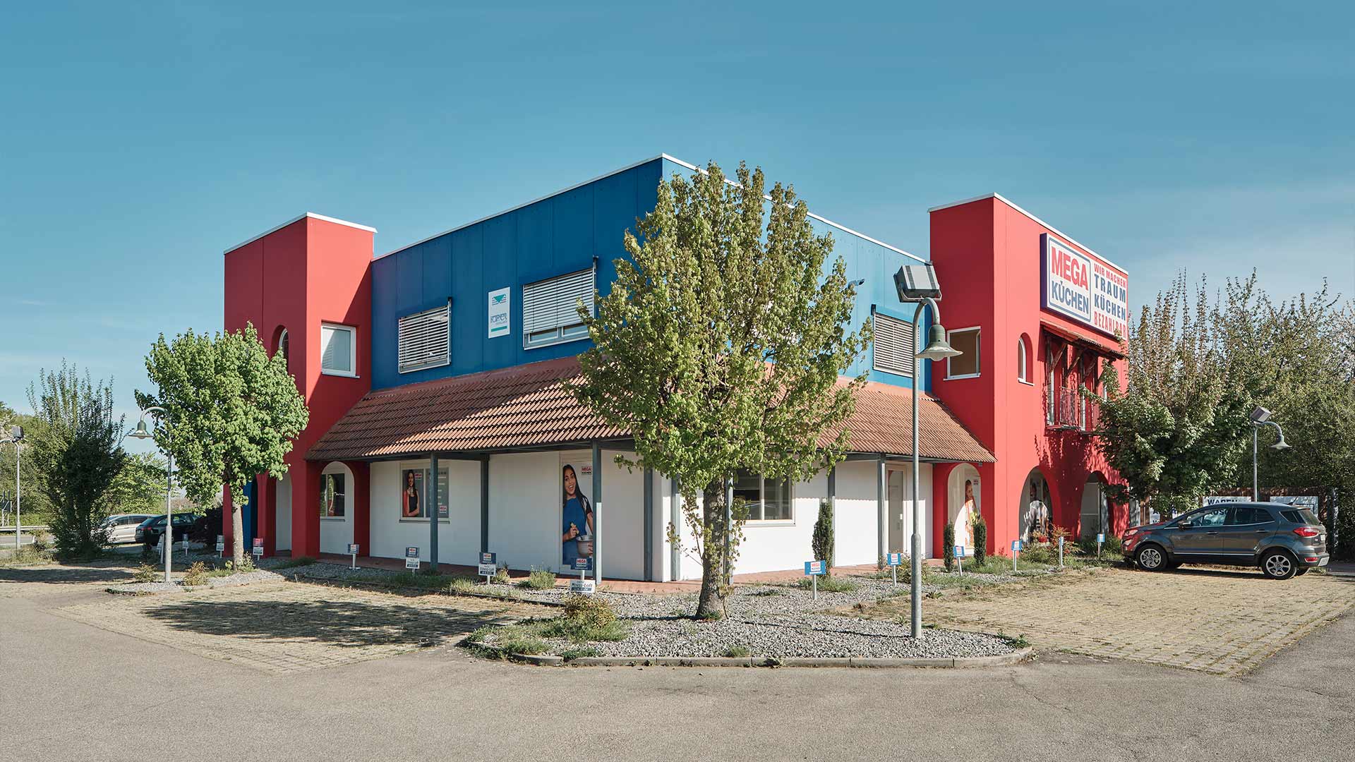 Ansicht auf Gewerbeimmobilie in Blau und rot mit Bäumen
