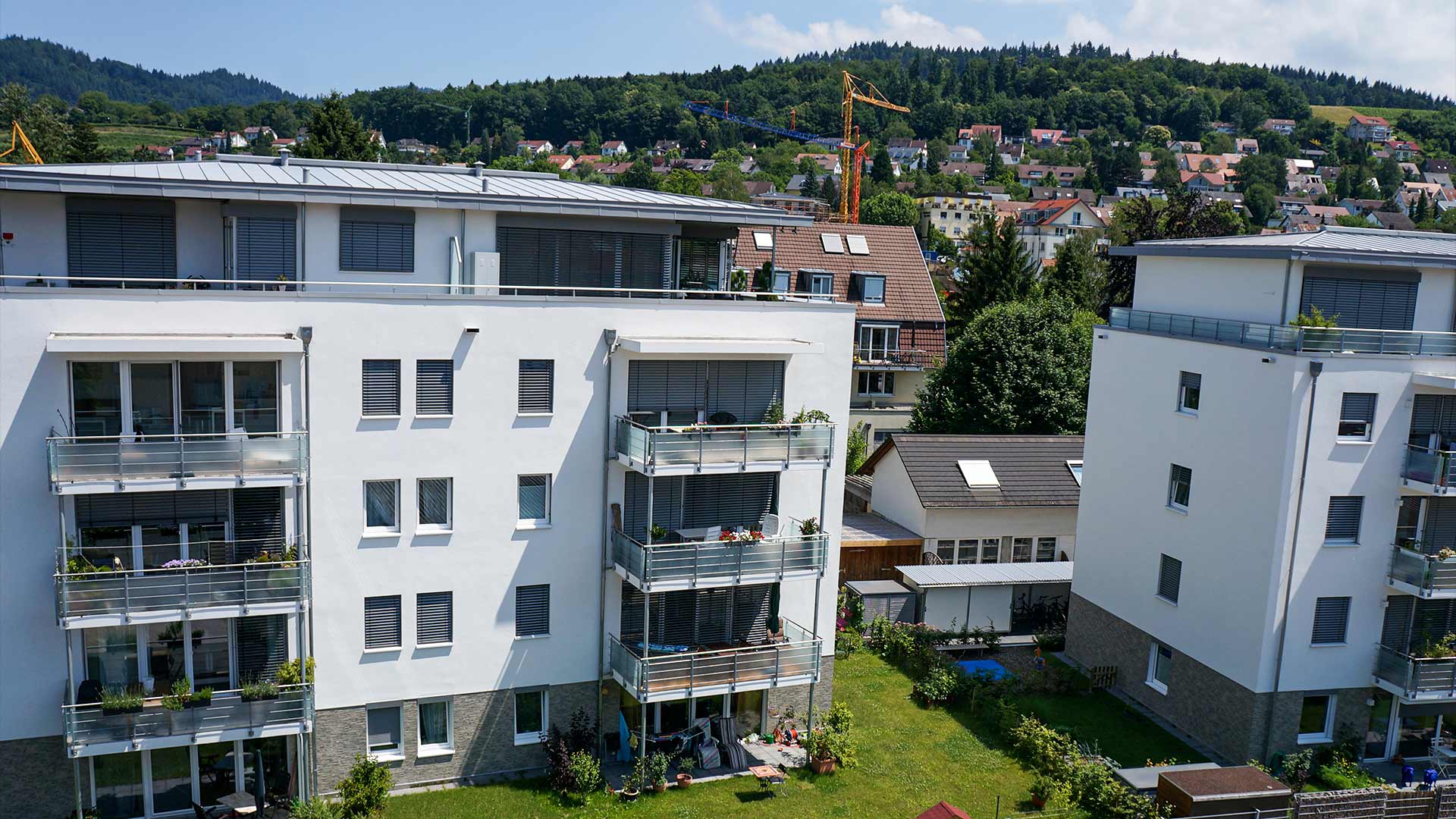 Frontalansicht auf ein Neubau-Wohngebäude mit Balkonen vor Bergen